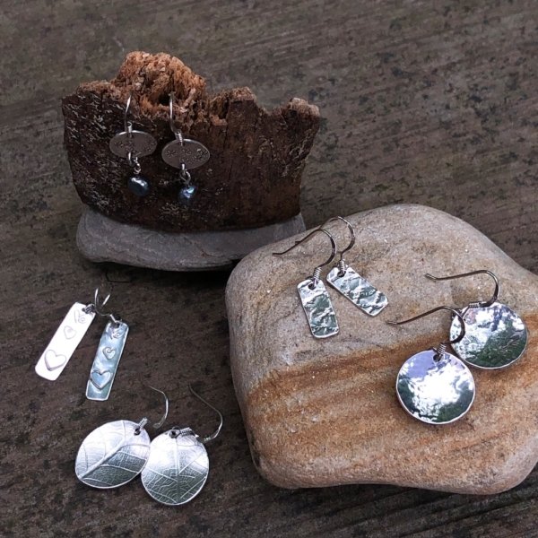 Silver earrings displayed on a stone and tree bark