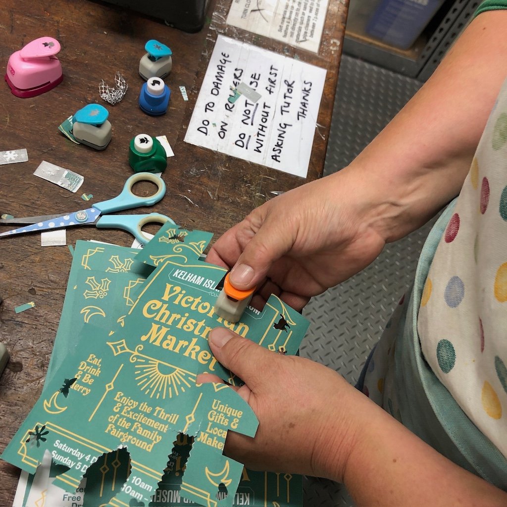 Student using craft punches to cut out paper shapes at the workbench