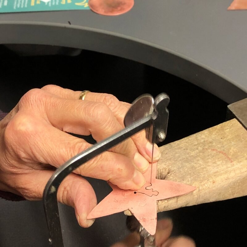 Hands saw piercing copper star on benchpeg