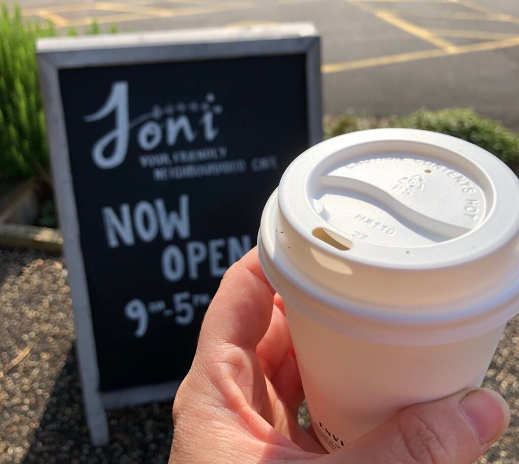 Holding a takeaway coffee cup near a chalkboard sign